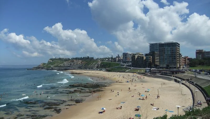 Newcastle Beach on a sunny day, with the city skyline behind the sand