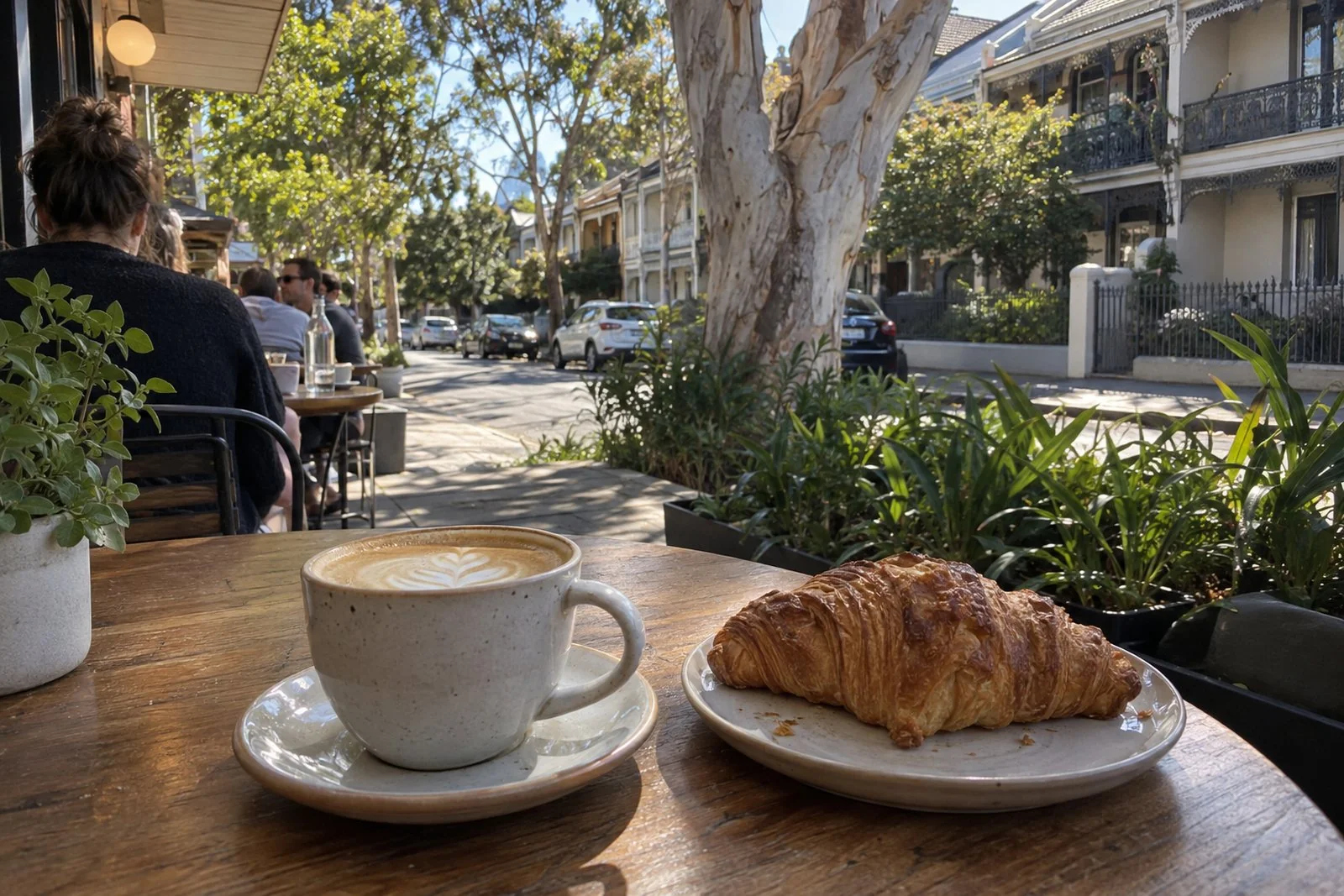 A flat white and a croissant on a footpath cafe table on a leafy Newcastle terrace street